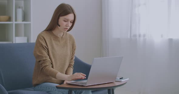 Woman Is Consulting Online, Using Video Call and Headphones, Talking and Looking at Screen of Laptop alt