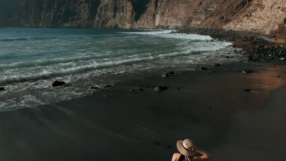 The Most Beautiful Aerial View: a Girl with a Hat and a Dress Runs Along the Black Beach, After