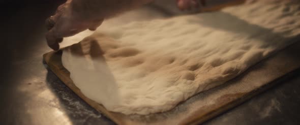 Chef preparing traditional italian al taglio pizza dough on a wooden surface. alt