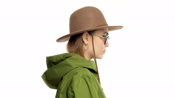 Woman in a Autumn Look in Studio in Green Parka and Hat Turns and Poses To the Camera alt