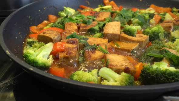 Cooking tofu with broccoli and vegetables in a pan at home. Vegetarian food alt