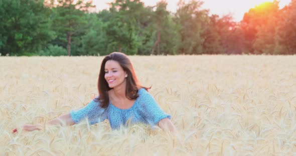 The Beautiful Young Girl Walks Across the Field of a Wheat at Sunset She is Wearing a Long Blue