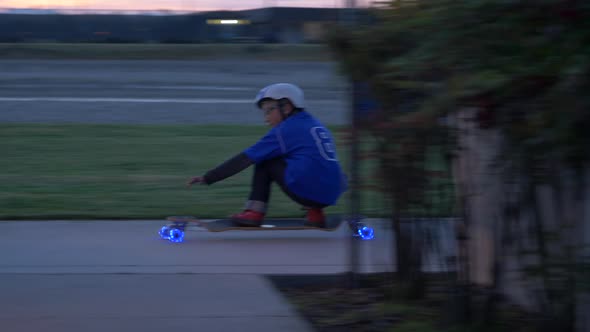 A boy rides a skateboard with led lights wheels in a neighborhood. alt