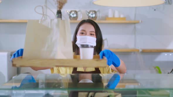 Attractive asian female cafe worker wears face mask and gloves giving takeaway