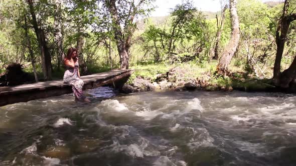 A Beautiful Girl Relaxes By the Lake Sitting on the Edge of a Wooden Bridge Swinging Her Feet at the alt