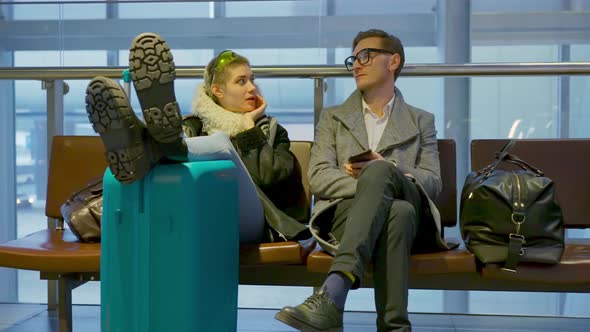 Young Adult Couple of Tourists Waiting for Their Flight Sitting with Suitcase and Talking