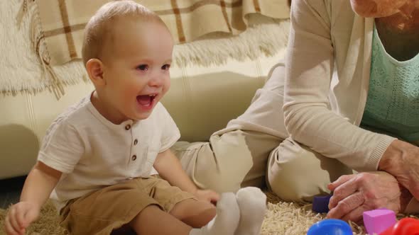 Funny Baby Boy Sitting on Floor with Grandmother and Laughing