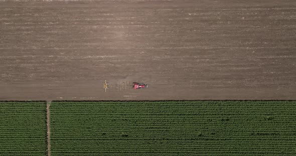 Red tractor flattening a field for seeding, Drone follow footage. alt