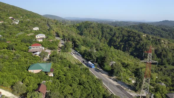 Blue Passenger Bus Drive Along Road Among Dense Green Forests in Highland alt