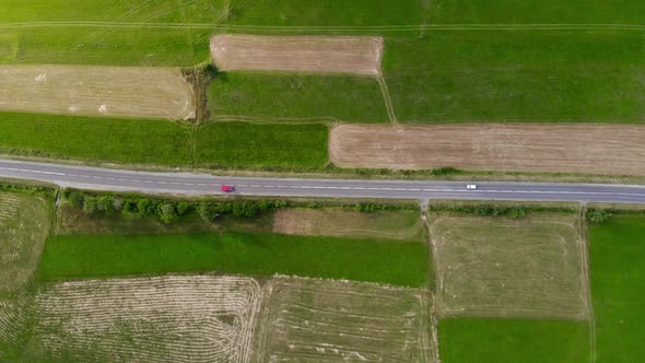 Aerial Drone Footage, Two Cars Driving on the Road Between the Fields