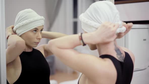 Reflection in Mirror of Young Concentrated Tattooed Woman Adjusting White Headscarf alt