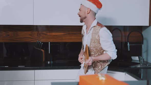 Handsome Young Man with Santa Hat Wiping Choping Board Like He is Playing Guitar alt