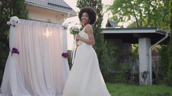 Back View of Cheerful African American Gorgeous Bride in White Dress Looking Back at Guests Turning alt