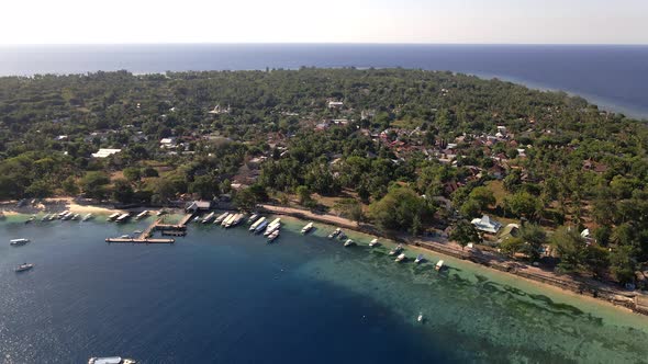 Aerial backward footage of beautiful Gili Air Island with trees,ocean shore,boats and hotels during alt