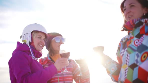 Three Caucasian Females in Ski Suits Smiling Laughing Drinking Wine From Glasses in Slowmotion alt