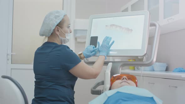 Girl Doctor Dentist Demonstrates a 3D Model of Teeth on a Touch Monitor alt