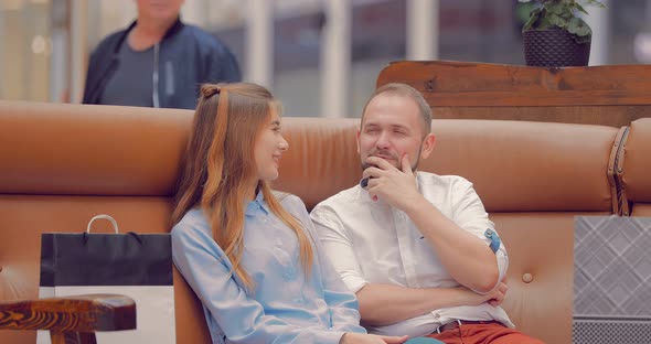 Man and a Girl are Sitting on a Sofa in a Mall and Discussing Something alt