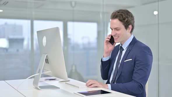 Happy Young Doctor Working on Desktop and Talking on Smart Phone  alt