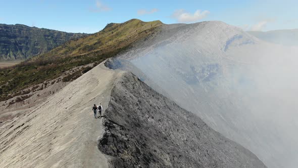 Hikers walking on ridge of Mount Bromo volcano alt