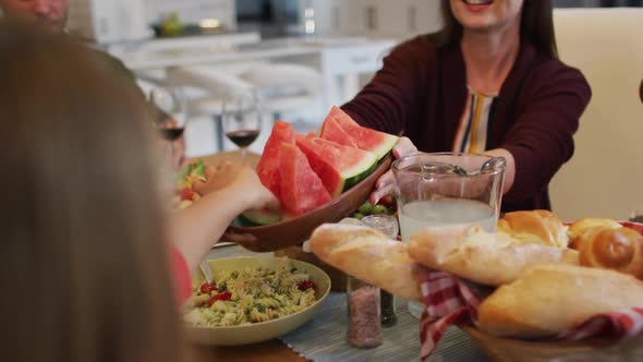 Smiling caucasian mother passing slices of melon to daughter at table before family meal alt