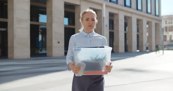 Upset Businesswoman Walking Outdoors with Box of Stuff Leaving Business Center alt