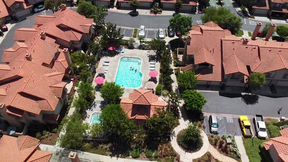 Aerial rotation around a community condo pool with swimmers. alt