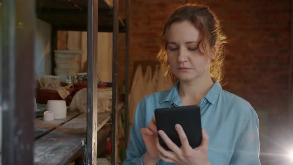 Slow Motion of Serious Girl Using Tablet in Pottery Workshop Looking at Ceramics alt
