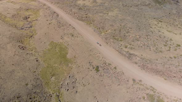 aerial shot following two mountain bikers climbing up a gravel road mountain pass alt