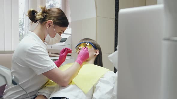 A Female Dentist in a Mask Is Curing a Patient in Special Glasses alt