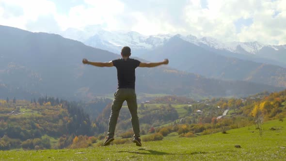 man jumps and claps his hands against background of autumn mountains. alt
