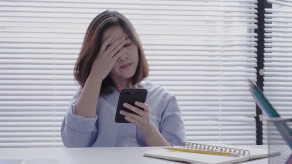 Young smiling asian woman working on laptop while sitting using phone for work in her home. alt