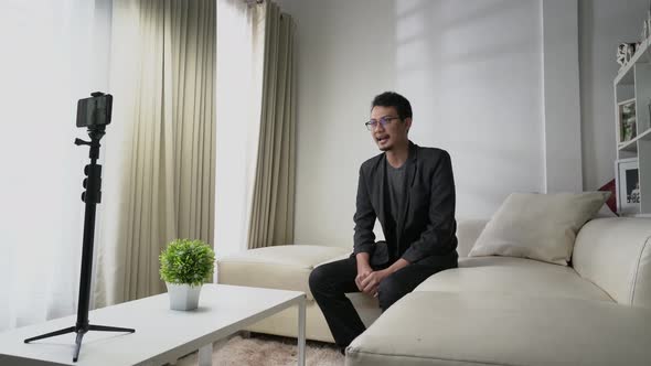 Asian man make a video call, interview, or conference sitting on a sofa with white concept room