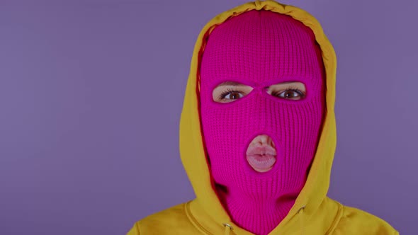 Unrecognizable Woman in Pink Balaclava Sending Blowing Kisses on Purple Background alt