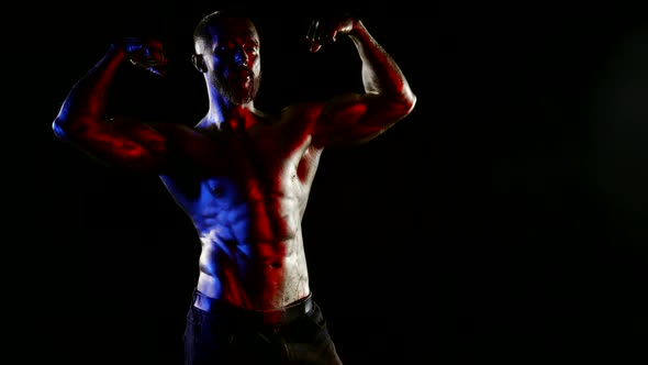 a Man with a Muscular Naked Torso and Metallic Golden Skin Poses and Demonstrates Biceps on a Black alt