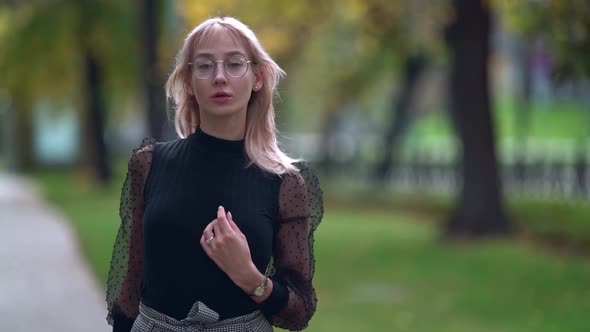 Young Romantic Lady Is Walking Alone in Park at Early Autumn, Looking at Camera and Smiling Broadly alt