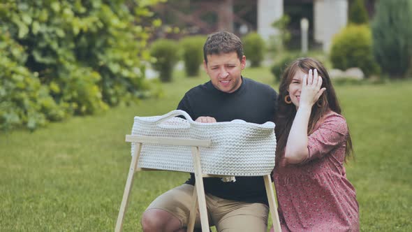 A Young Couple Looks at Their Newborn Baby in a Cradle in the Garden alt