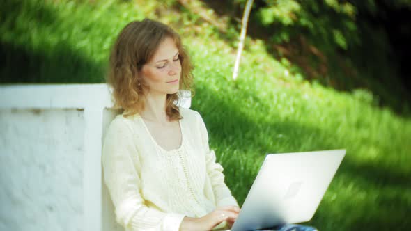 Beautiful Woman Working on a Laptop on a Wooden Bench in the Park