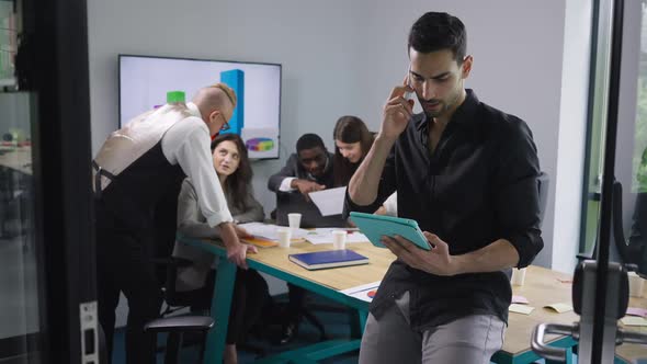 Serious Confident Middle Eastern Man Talking on Phone Analyzing Emarket on Tablet As Caucasian and alt