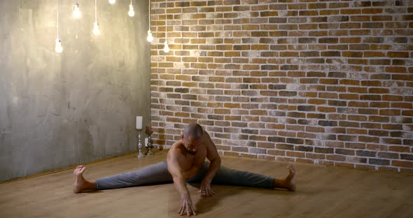 Muscular Man Is Stretching Legs Sitting in a Split on Floor in Home in Evening alt