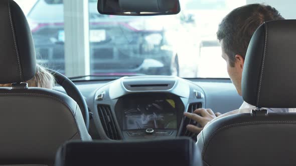 Funny Dad with His Daughter Sit in the Front Seats and Look at the Small Screen of the Car