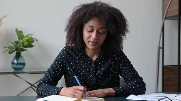 Smart Confident Darkskinned Student Girl Dressed in a Stylish Shirt Sits at Her Desk with a Notebook alt