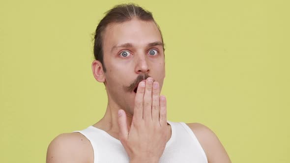 Closeup Astonished Young Man Closing His Mouth with Hand in Surprise Over Yellow Background Slomo alt