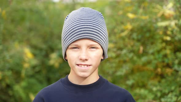 Smiling boy in striped hat standing in park look at camera.