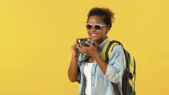 African American woman tourist wearing sunglasses and backpack taking photos on camera