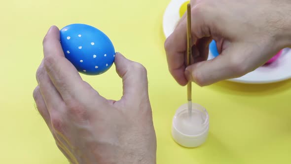 Happy Easter Close Up. White man painting a blue Easter egg in polka dot with white acrylic color