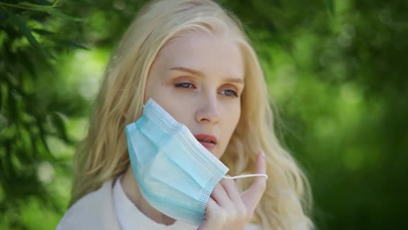 Beautiful Blonde Woman Takes Off the Medical Mask and Sniffs the Flower