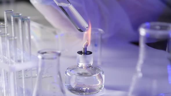 Close-up of hand of medical scientist test tube with a solution over burner fire alt