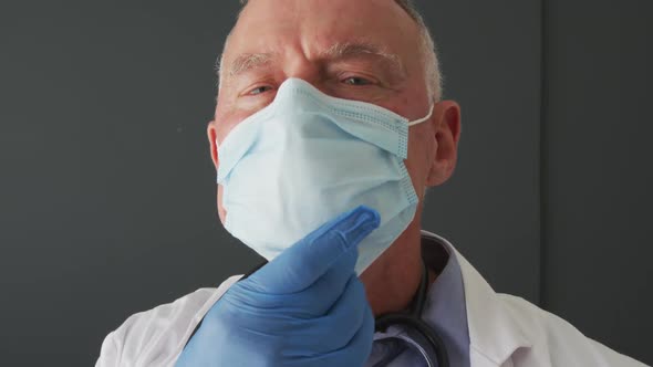 Portrait of caucasian senior male doctor lowering his face mask and smiling alt