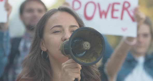 Close-up of Young Caucasian Feminist Shouting Through Megaphone. Protest Leader Encouraging alt