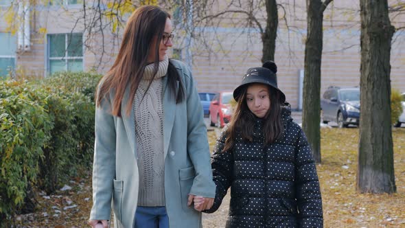 Mom and Daughter of a Student in Elementary School Go Home Together After School Through the Autumn